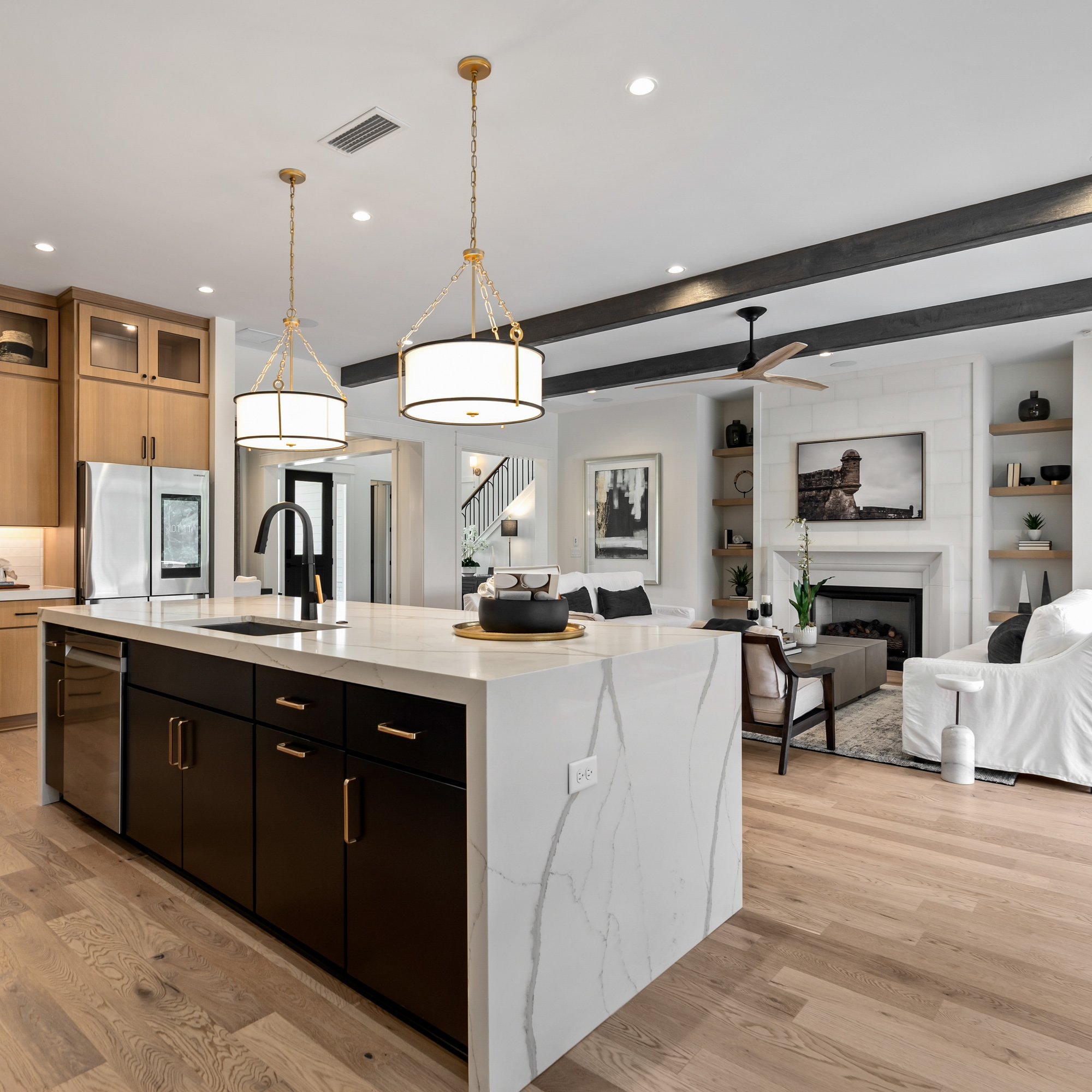 Home interior showing a kitchen and living room. The kitchen features a waterfall island with veined marble and dark cabinets.